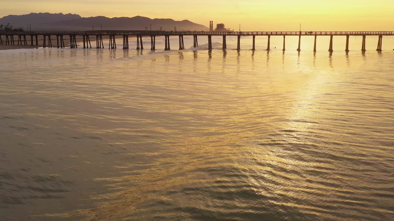 金色的海浪滚动在海滩旁边的长码头在一个金色的日出视频素材