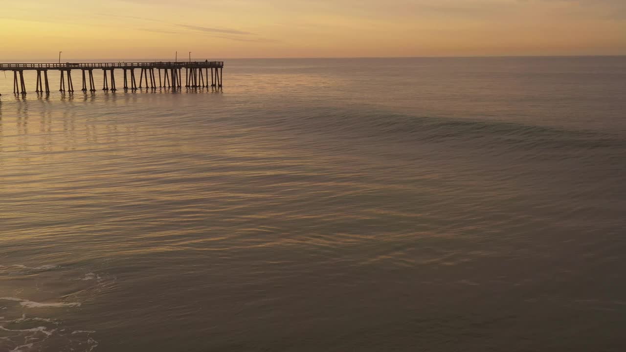 金色的海浪滚动在海滩旁边的长码头在一个金色的日出视频素材