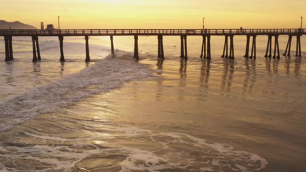 金色的海浪滚动在海滩旁边的长码头在一个金色的日出视频素材