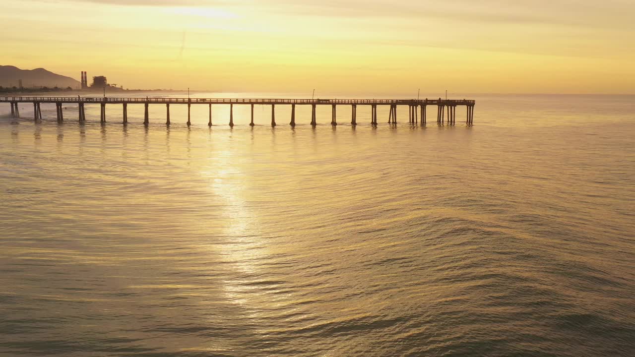 金色的海浪滚动在海滩旁边的长码头在一个金色的日出视频素材