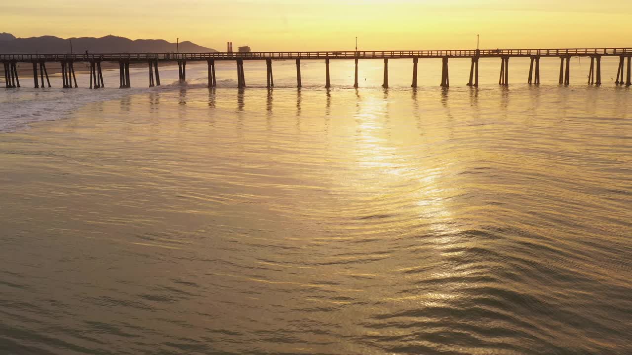 金色的海浪滚动在海滩旁边的长码头在一个金色的日出视频素材