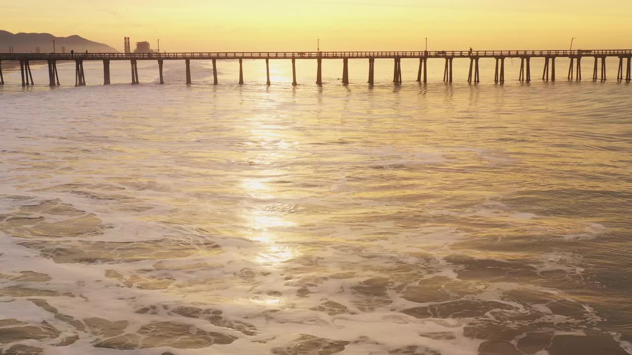 金色的海浪滚动在海滩旁边的长码头在一个金色的日出视频素材