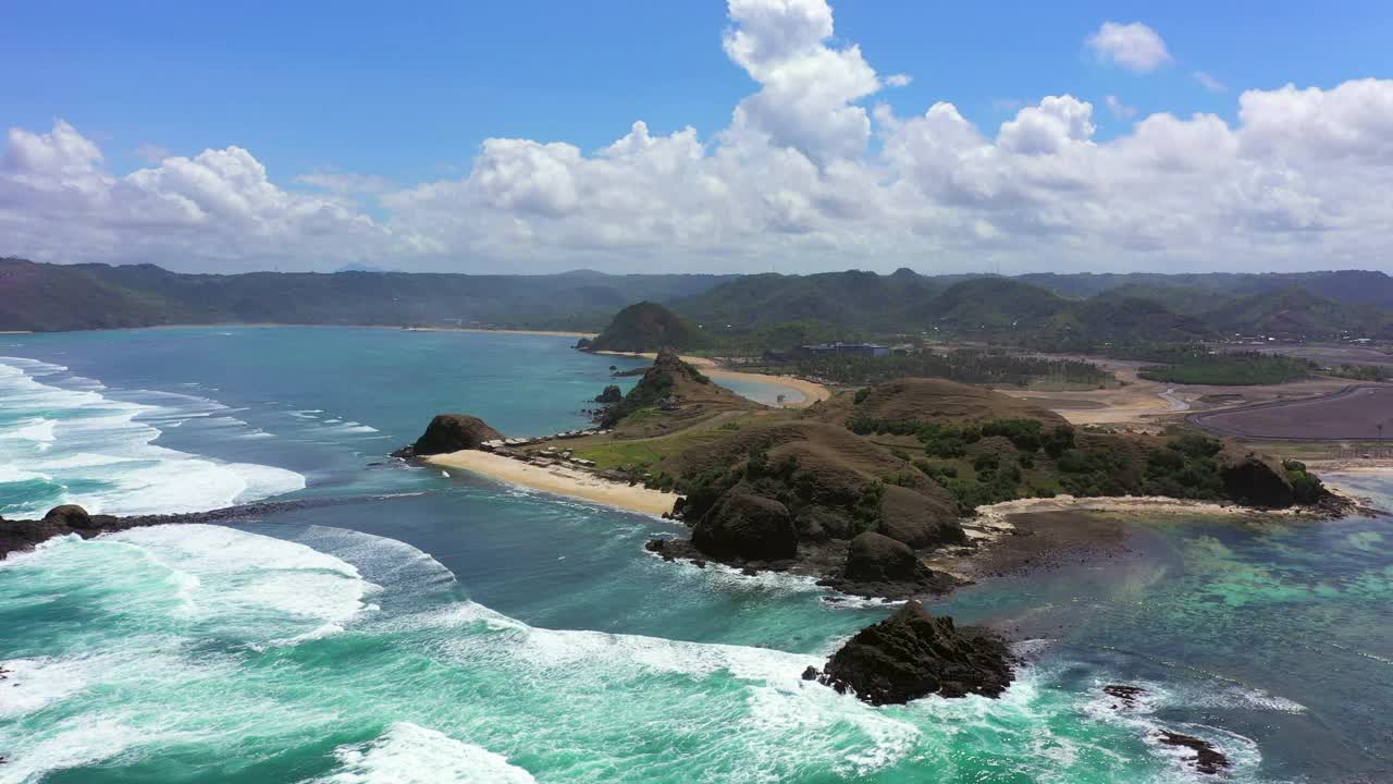 空中平移拍摄的山在海滩上对多云的天空，无人机在阳光灿烂的日子飞越波浪的海洋-龙目岛，印度尼西亚视频素材