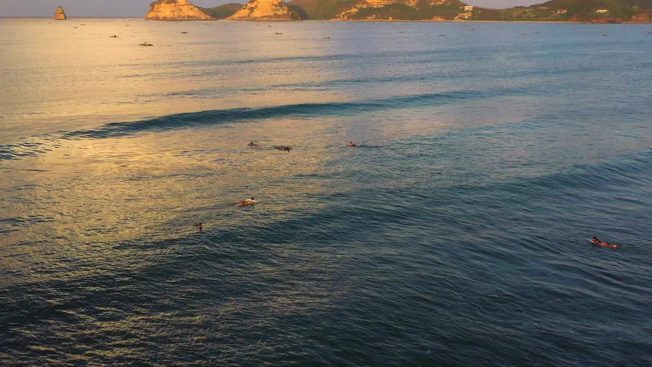 航拍:在印度尼西亚龙目岛度假期间，冲浪者用冲浪板在海浪上游泳的无人机拍摄视频素材