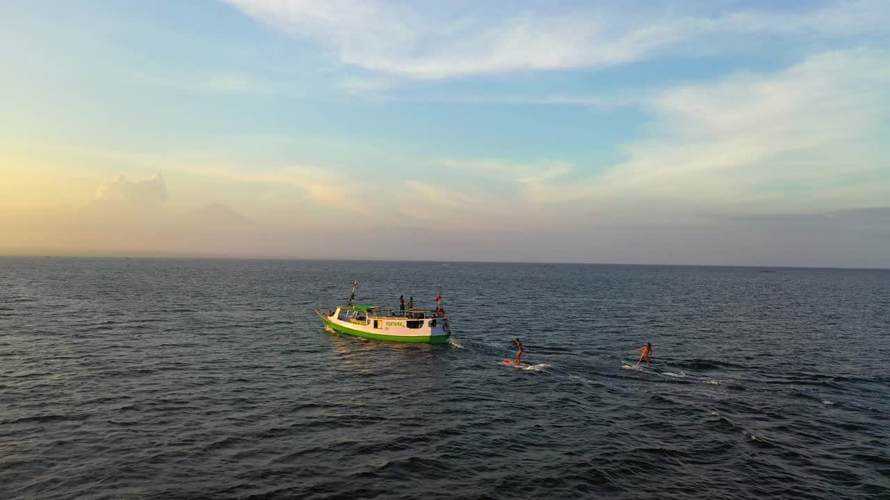 航拍冲浪者冲浪背后的航海船只，无人机在日落期间飞越海洋-龙目岛，印度尼西亚视频素材