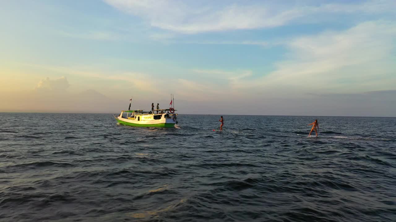 空中向前拍摄的女性冲浪者在天空中云下的船后面冲浪-印度尼西亚龙目岛视频素材