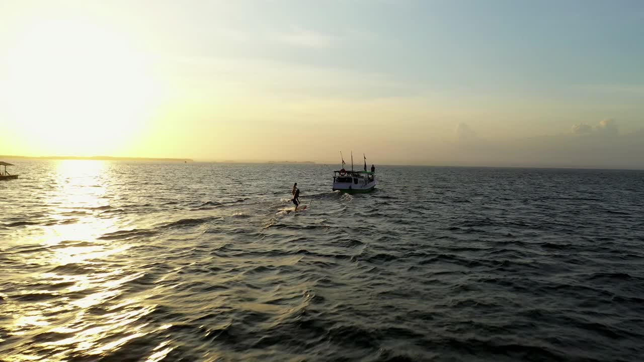 航拍的剪影的人在海上冲浪船后面，无人机在日落期间飞越海洋-龙目岛，印度尼西亚视频素材