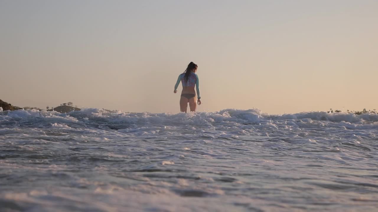 慢动作后视图的妇女冲浪海浪在日落期间-龙目岛，印度尼西亚视频素材