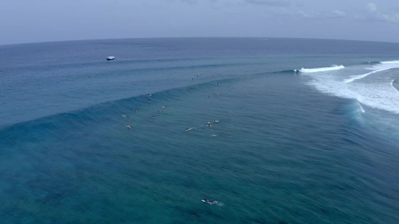 在多云的天空下，人们在波浪形的大海中游泳和冲浪的空中锁定镜头——马尔代夫的thulushoo视频素材