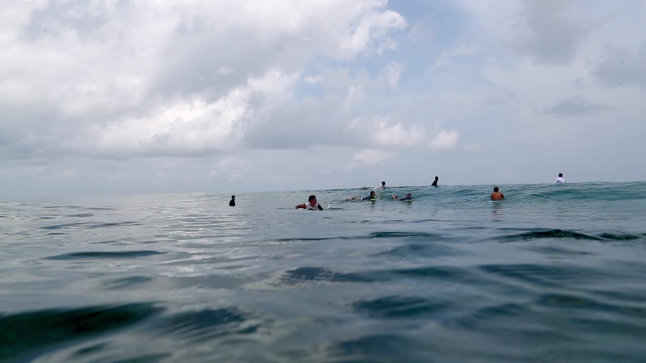 慢镜头的男性冲浪者游泳与冲浪板在海浪在多云的天空下- thulushoo，马尔代夫视频素材