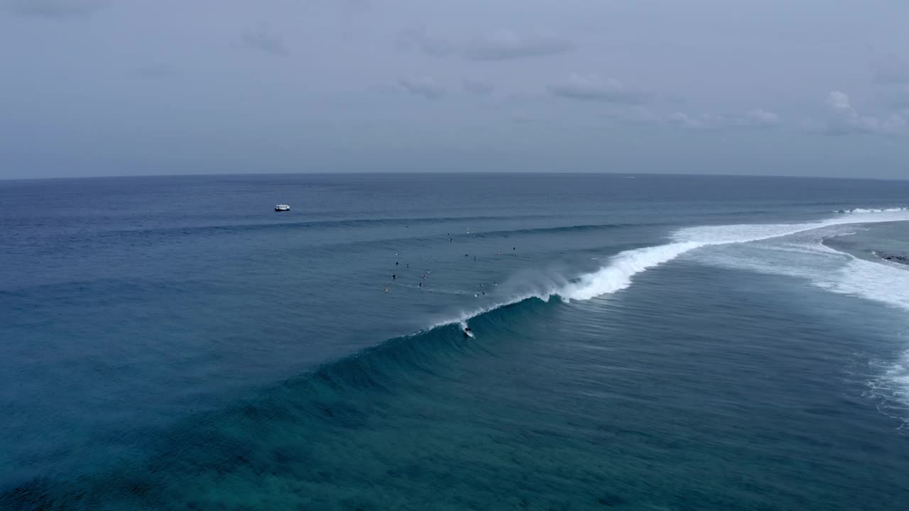 航拍的游客在海浪上冲浪，无人机在多云的天空下向后飞行——马尔代夫的thulushoo视频素材