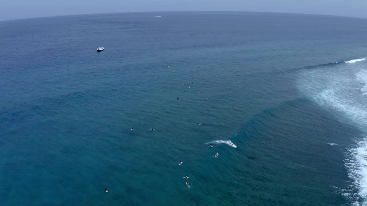 空中向后拍摄的人们在海上冲浪的海浪对着天空——马尔代夫的thulushoo视频素材