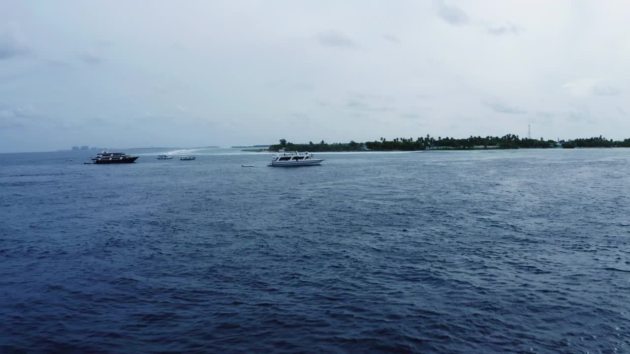 在多云的天空下，漂浮在海上波浪上的白色航海船只的空中前进镜头-马尔代夫的thulushoo视频素材