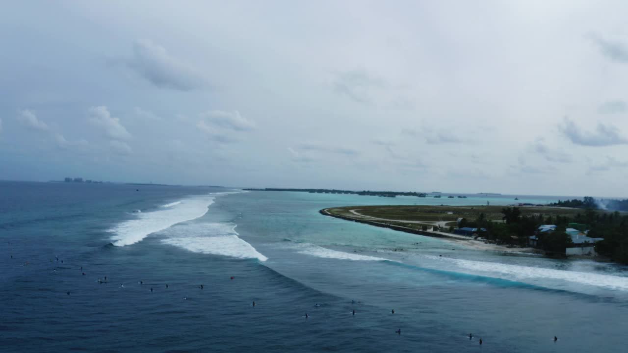 空中平移风景拍摄的岛屿在云下，无人机飞过在海上冲浪的人- thulushoo，马尔代夫视频素材