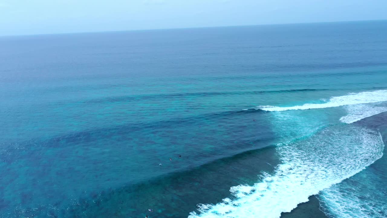 空中平移向后拍摄的游客冲浪者在海浪上冲浪对着天空-马尔代夫的thulushoo视频素材