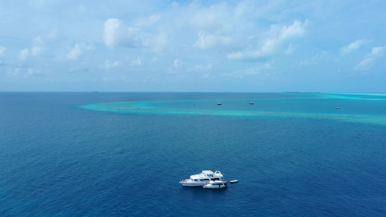 空中拍摄的白色航海船只漂浮在蓝色的大海上，无人机在天空的云层下向前飞行-马尔代夫的thulushoo视频素材