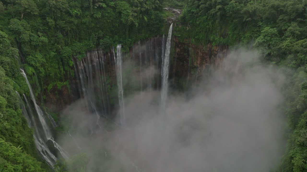 空中拍摄的风景著名瀑布流动在岩层，无人机飞行向前在云-爪哇，印度尼西亚视频素材