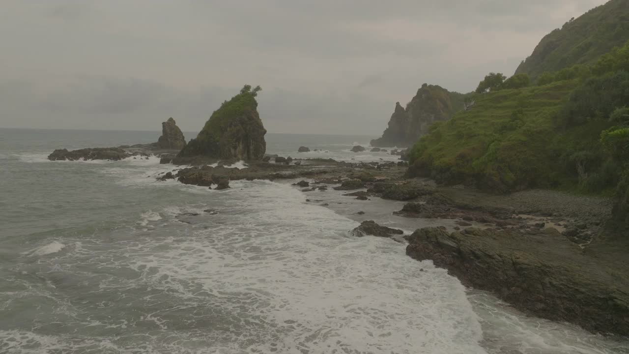 空中拍摄的天然岩石岩层对多云的天空，无人机飞行向前在波浪的海-爪哇，印度尼西亚视频素材