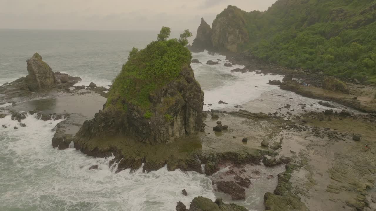 空中平移拍摄的绿色植物在岩石形成在海上-爪哇，印度尼西亚视频素材