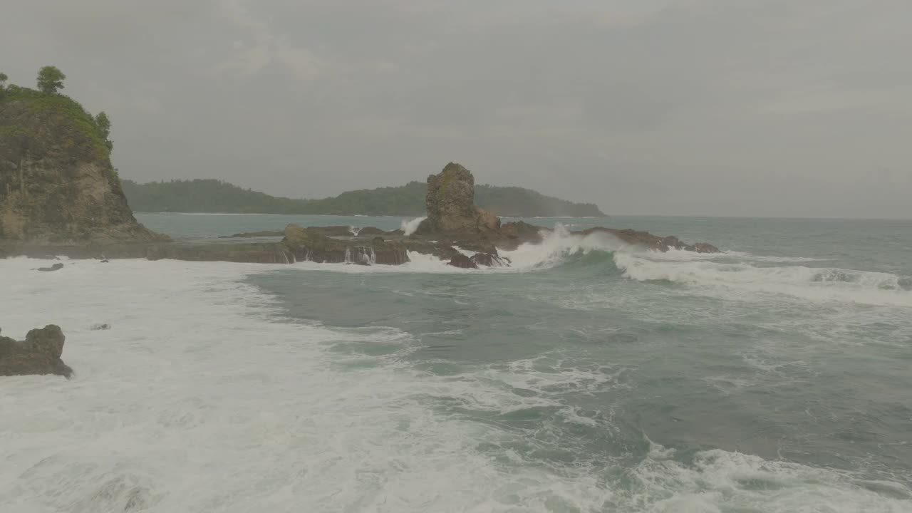 在多云的天空中，海浪溅在岩石上的空中向前拍摄-印度尼西亚爪哇视频素材