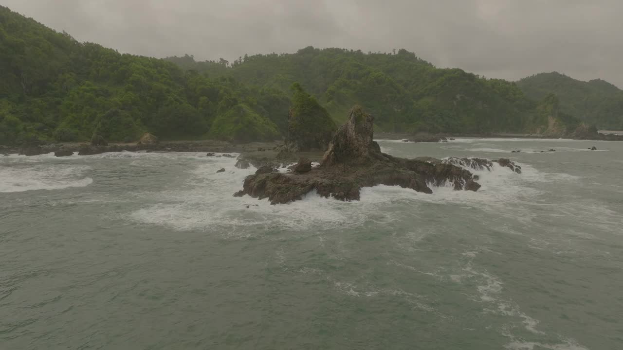 空中向前拍摄的海浪飞溅在岩石上，对着天空中的云-爪哇，印度尼西亚视频素材