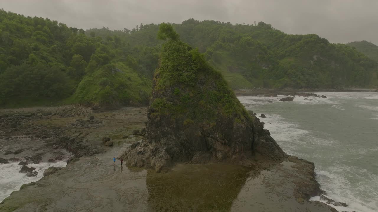 空中向后拍摄的游客在海洋岩层对多云的天空-爪哇，印度尼西亚视频素材