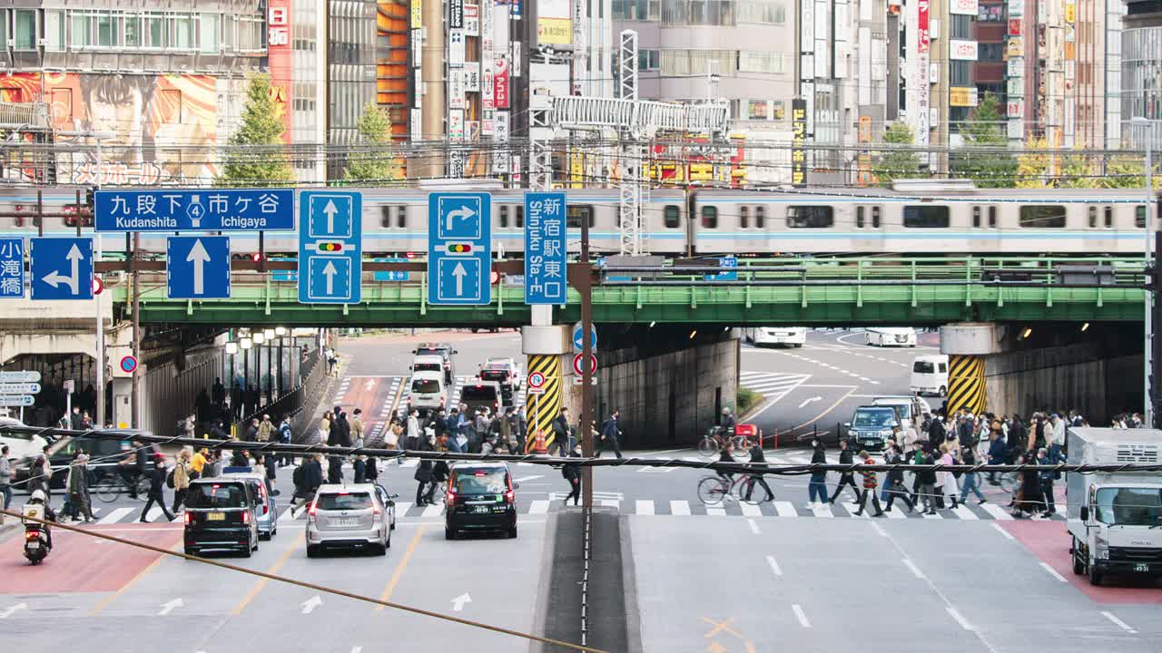 汽车、公共汽车交通运输在道路十字路口，地铁列车在高架轨道上，日本人在日本东京新宿区走过十字路口。亚洲交通，亚洲城市生活。视频素材