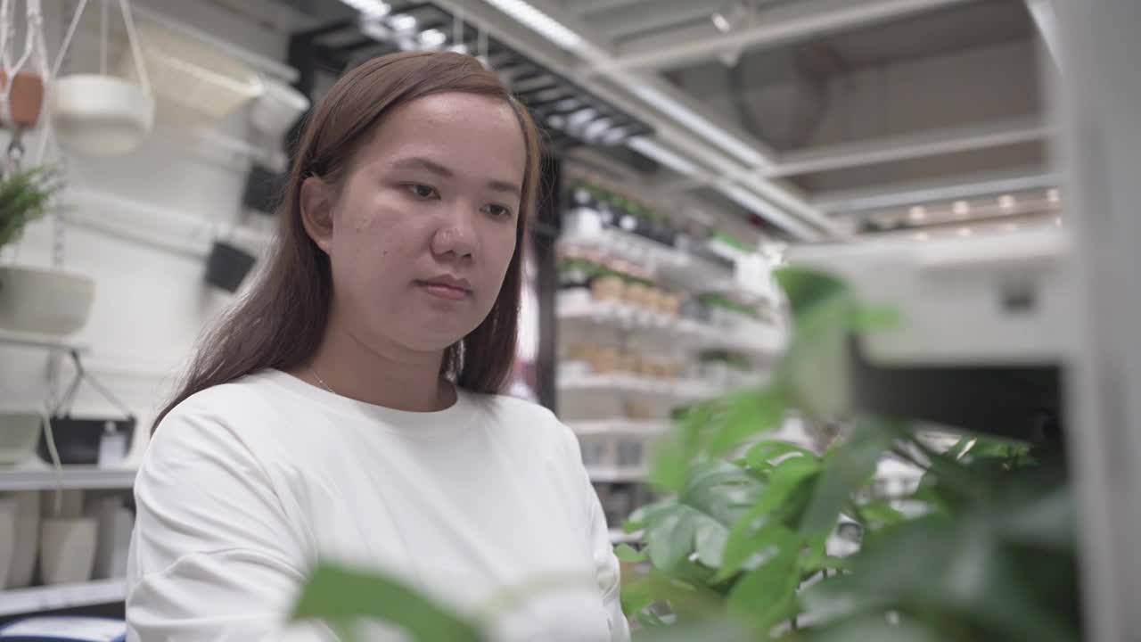 年轻女子购买盆栽植物。寻找室内植物装饰视频素材