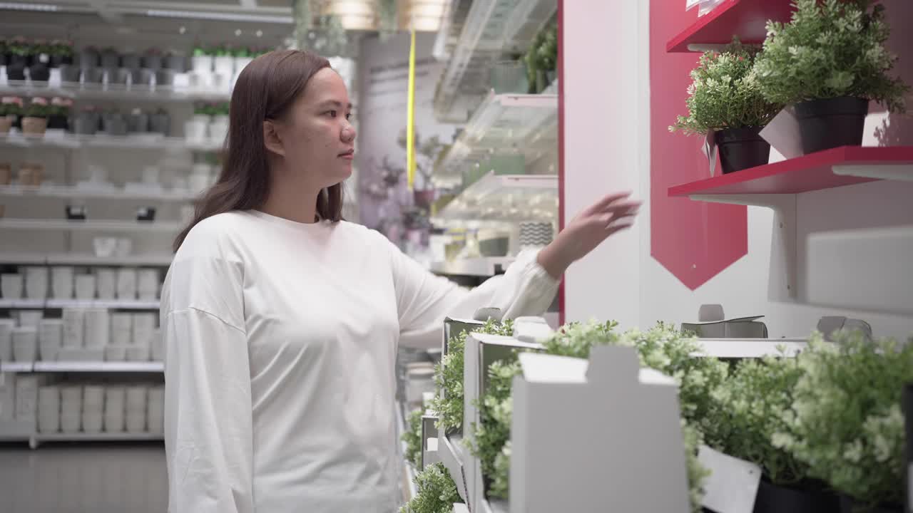 年轻女子购买盆栽植物。寻找室内植物装饰视频素材