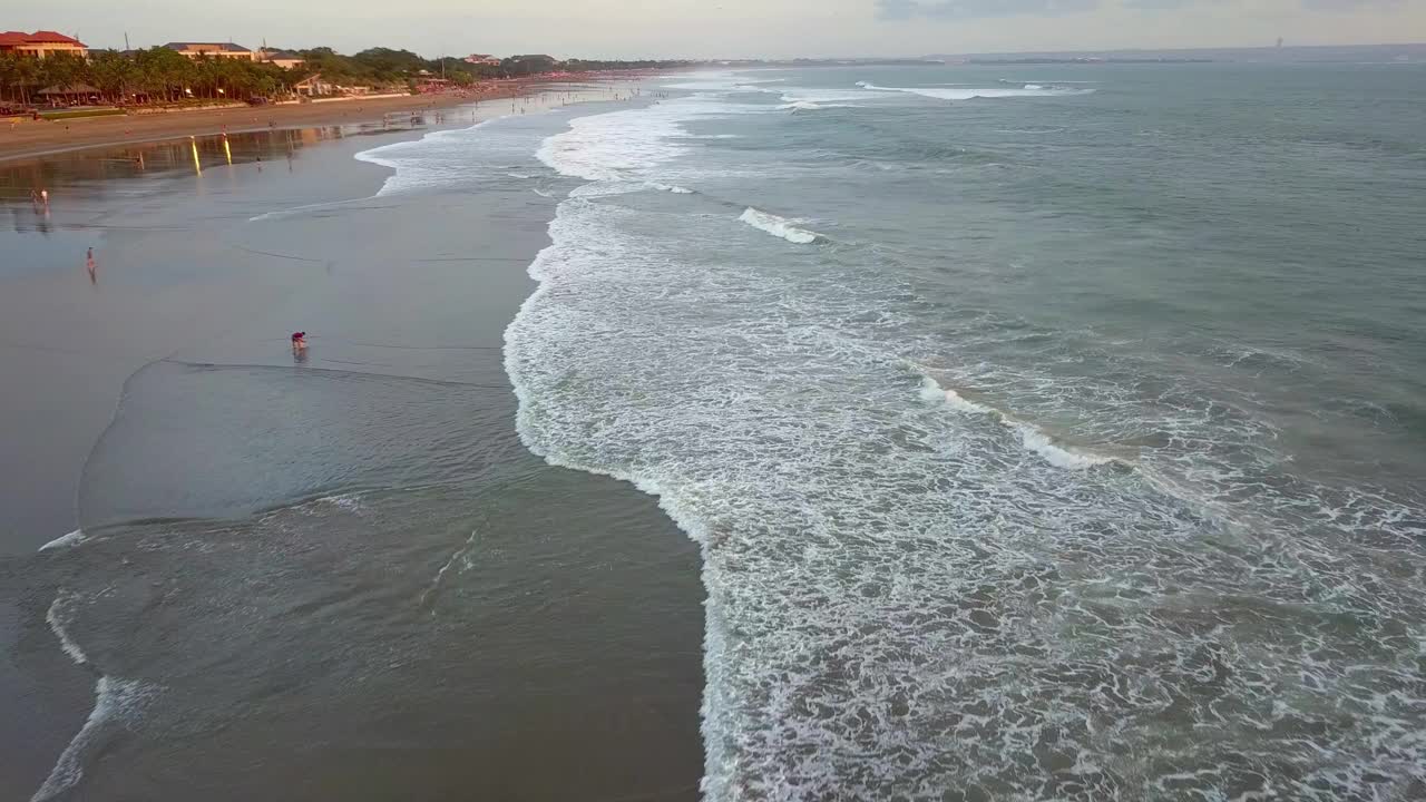 无人机拍摄的日落，海浪在印度洋破碎。夕阳在海浪上冲刷着沙滩。空中日落。海滩上的人，自然海景。天堂巴厘岛，印度尼西亚，亚洲的海湾。视频下载