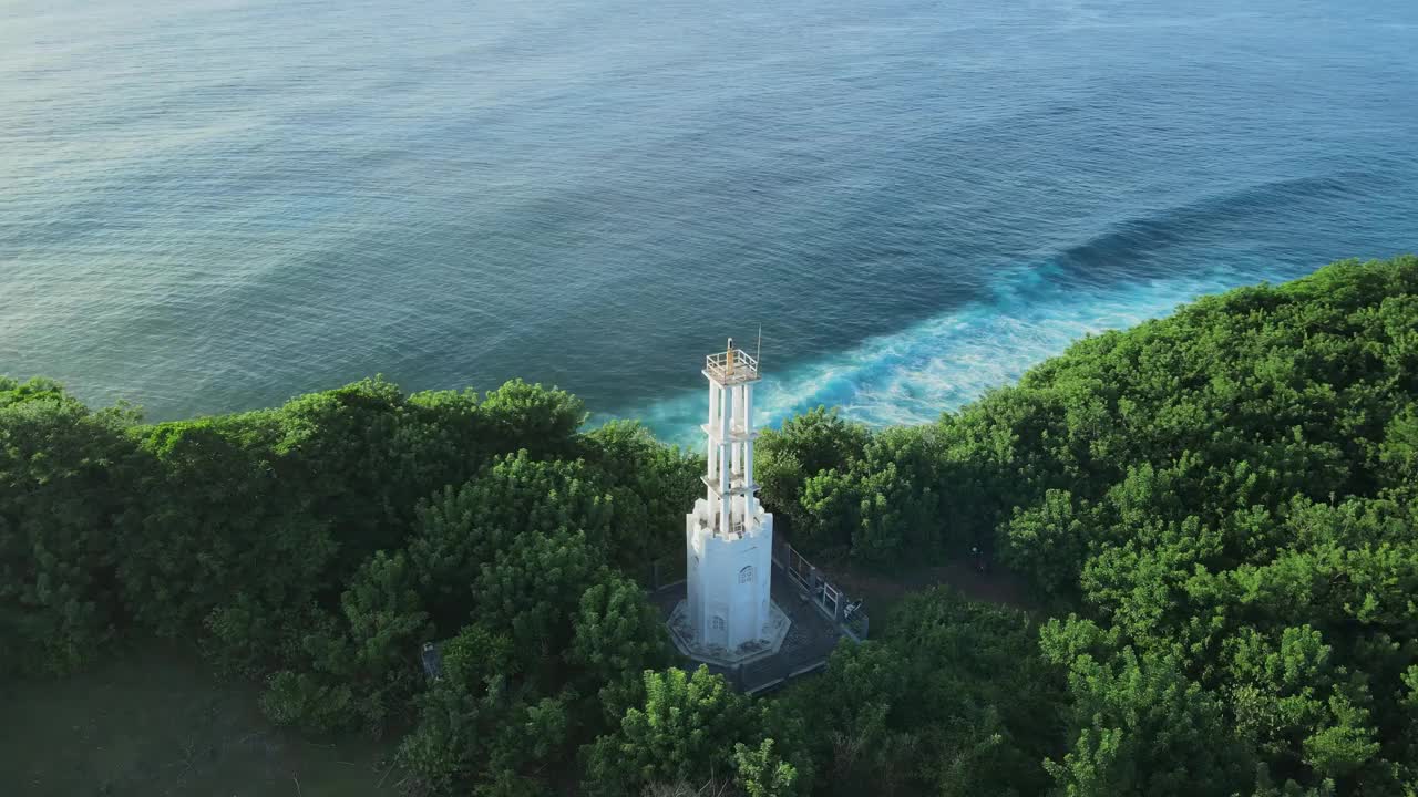 鸟瞰巴厘岛乌鲁瓦图风景优美的海岸线，有灯塔、阳光和海浪视频素材