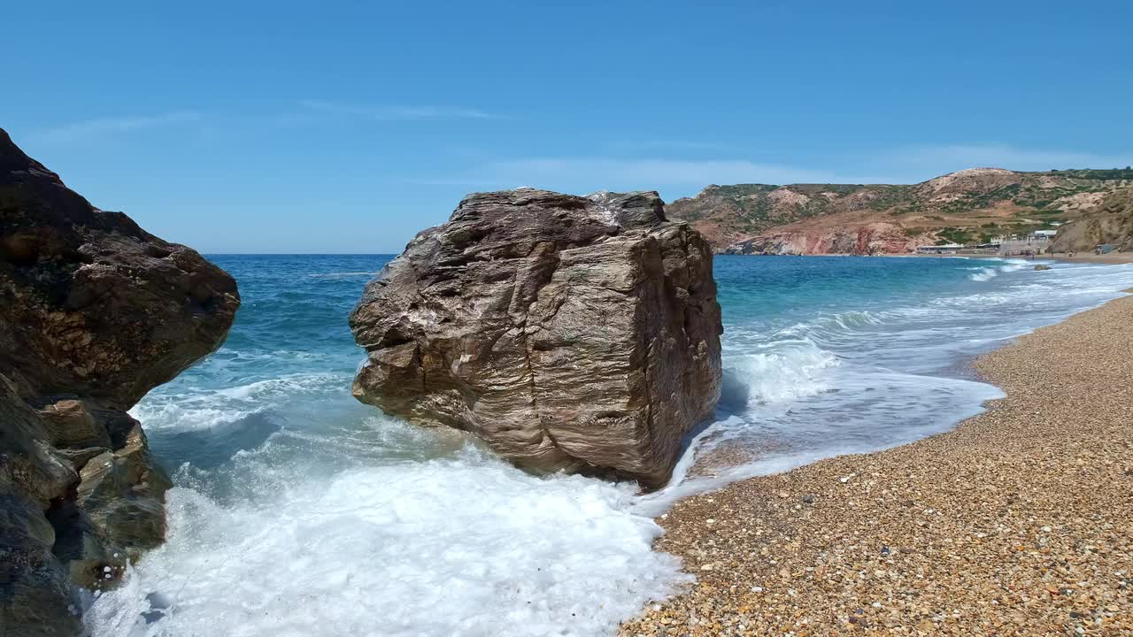 蓝色的海浪拍打着海滩上黄色的鹅卵石和黑色的岩石。永恒冥想的概念，放松和度假。视频素材