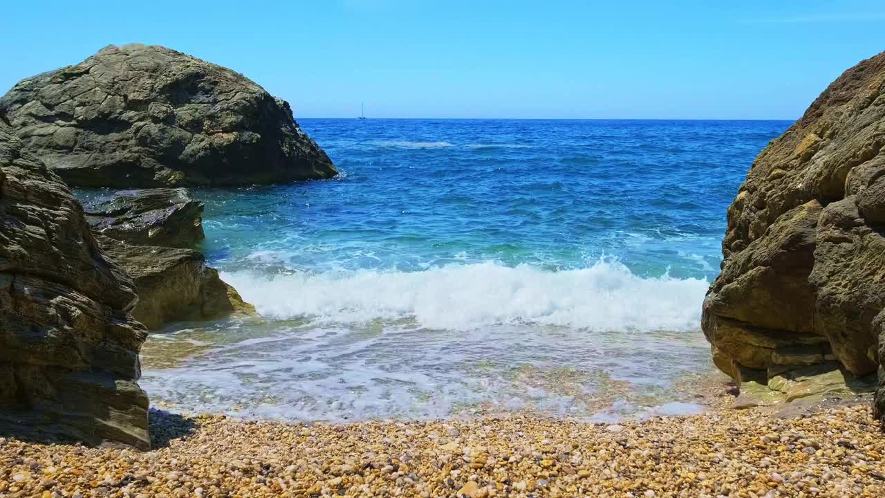 蓝色的海浪拍打着海滩上黄色的鹅卵石和黑色的岩石。永恒冥想的概念，放松和度假。视频素材