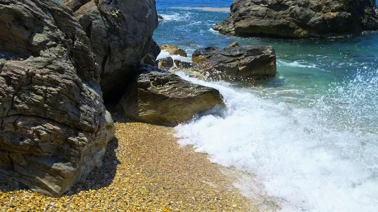 白色浪花拍打着沙滩上黄色的鹅卵石和黑色的岩石。永恒冥想的概念，放松和度假。视频素材