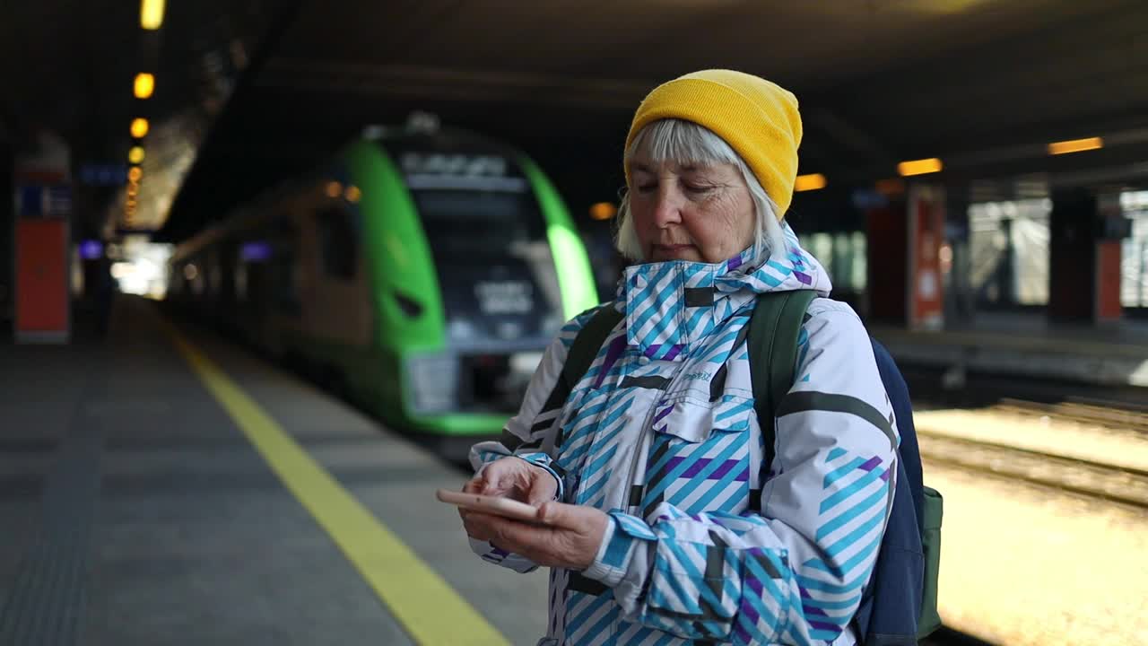 50多岁的女子在火车站用智能手机旅行。年长的白人旅行者在终点站或火车站用手机应用程序查询登机时间。视频素材