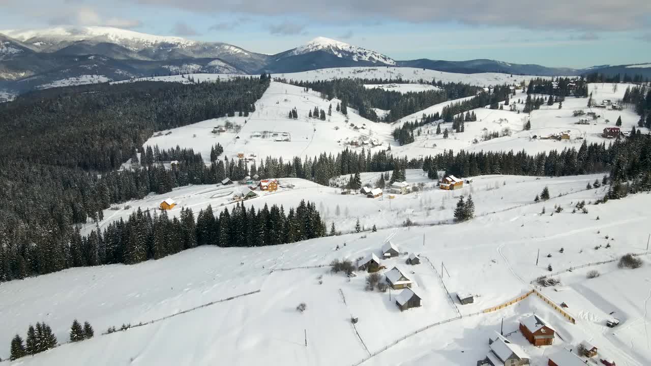 冬季景观，在寒冷的山区积雪覆盖的森林之间，偏远定居点的小乡村房屋视频素材