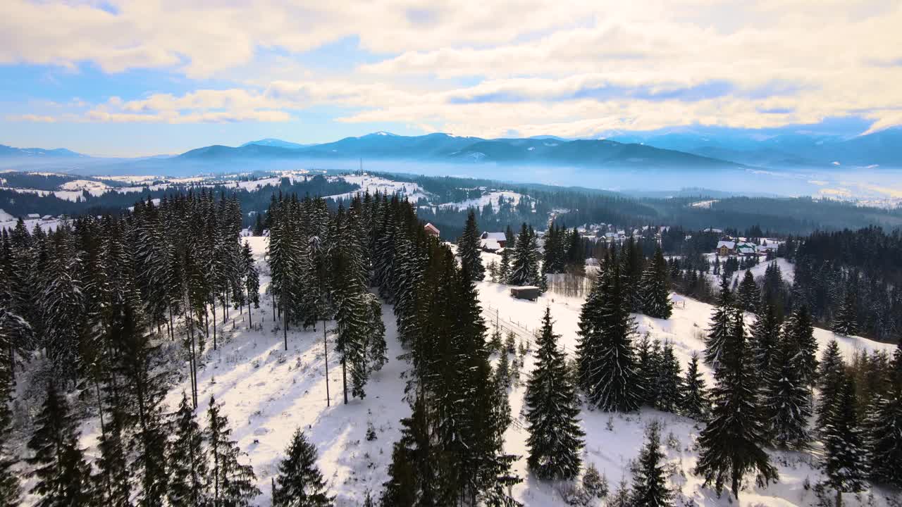 在寒冷的山区，白雪覆盖的森林之间有小村庄的冬季景观视频素材