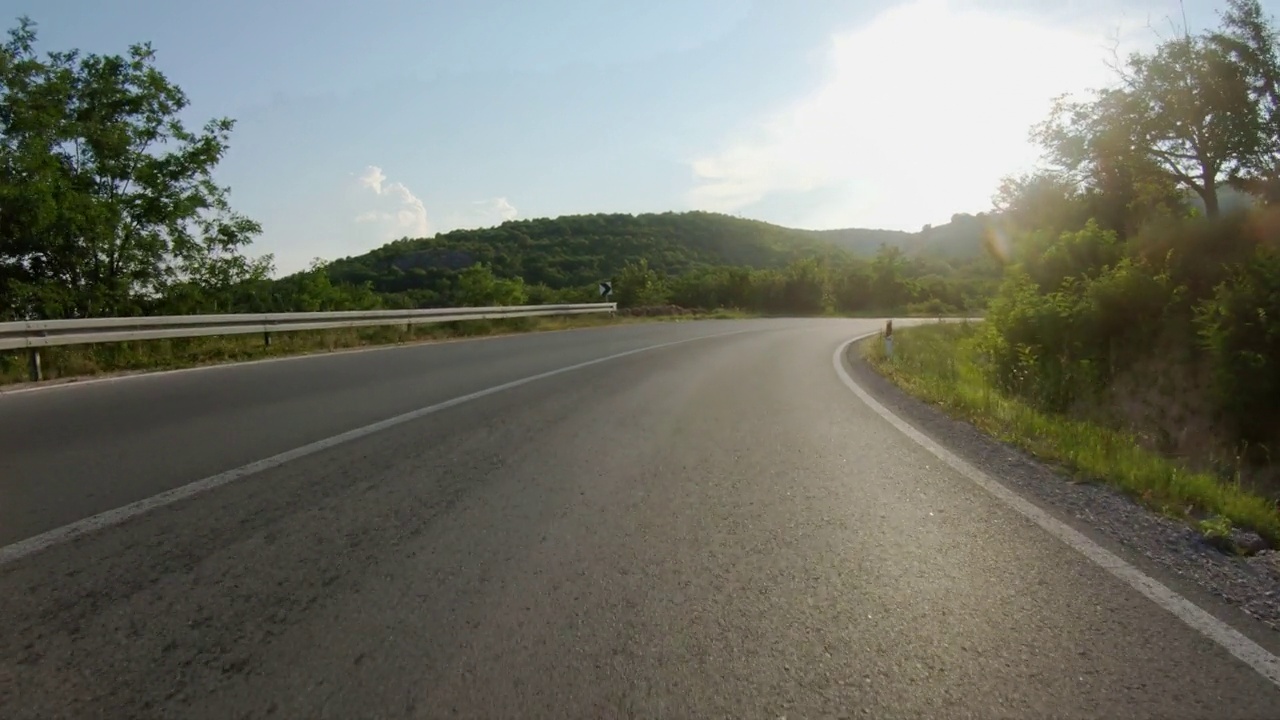 日落时分，在蜿蜒的道路上乘汽车或摩托车缓慢骑行。蓝天，夏日时光。观点拍摄视频下载