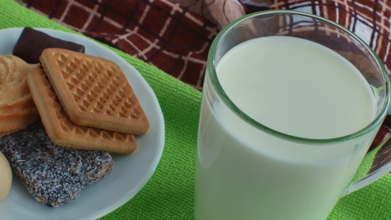 一杯牛奶，一个装着糖果和饼干的盘子，绿色餐巾纸上的特写。甜的甜点。糖对健康危害的概念视频素材