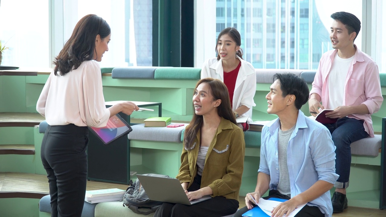 一群快乐的亚洲青年大学生用笔记本电脑进行头脑风暴和讨论，在大学图书馆通过网络和课本查找信息。科技学科视频素材