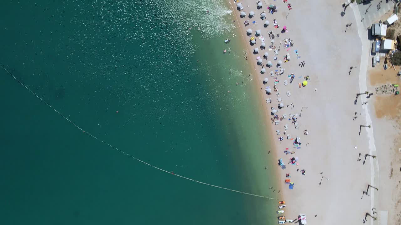 Drone shot of a Zrće beach in Pag, Croatia. Beautiful white pebble shore full with beach clubs, lounge chairs and tourists enjoying in the clear, blue water视频下载