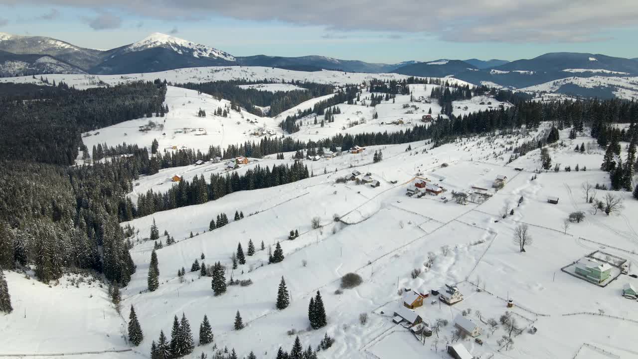 在寒冷的山区，白雪覆盖的森林之间有小村庄的冬季景观视频素材