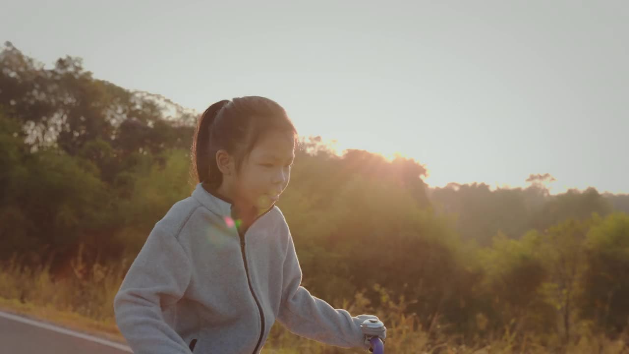 快乐的兄弟姐妹亚洲女孩骑自行车，享受与自然一起日出在早上的时间。孩子们在大自然的清新中户外运动。健康生活方式的概念。视频下载