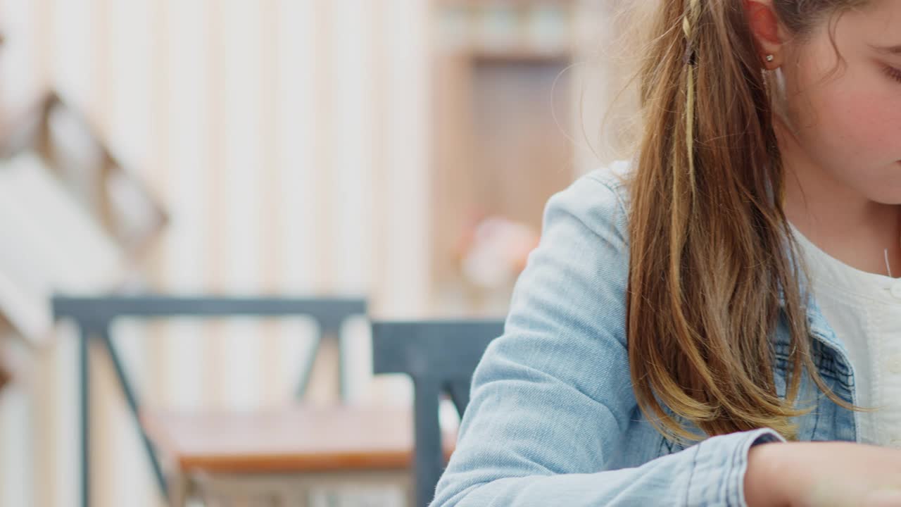 一个白人小学女生在学校空闲时间在她的课桌上看书的特写。视频素材