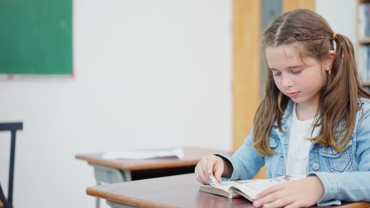 一个白人小学女生在空闲时间坐在学校图书馆看书的特写。视频素材