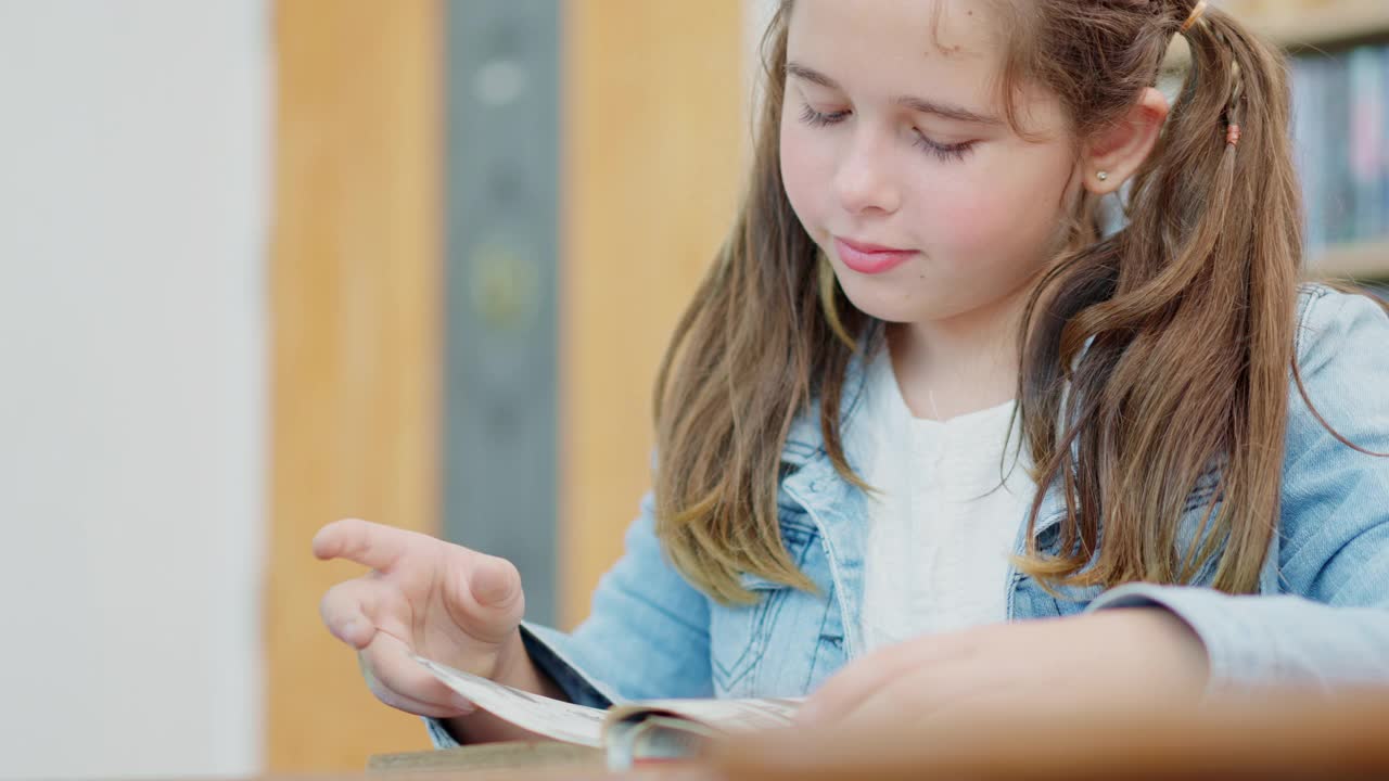 一个白人小学女生在学校空闲时间在她的课桌上看书的特写。视频素材