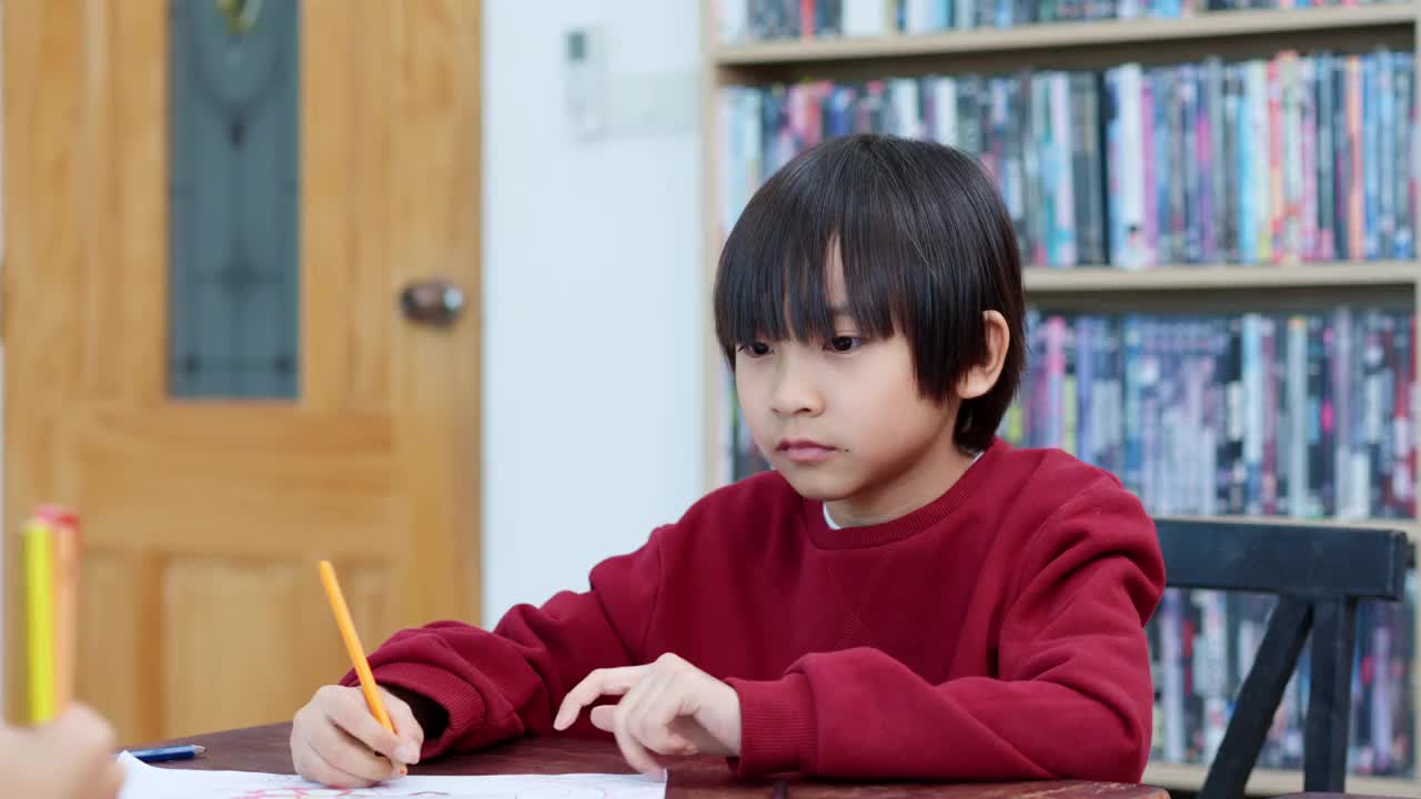 图为，一名亚裔小学生在美术课上与多种族的朋友一起学习时，正拿着彩色铅笔在纸上画画。视频素材