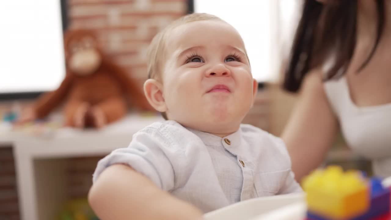 可爱的幼儿拿着塑料积木坐在幼儿园的桌子上视频素材