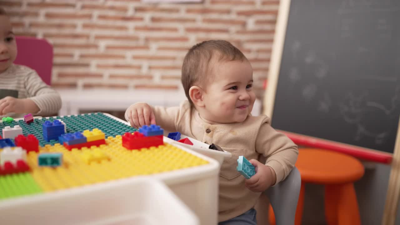 可爱的幼儿拿着塑料积木坐在幼儿园的桌子上视频素材