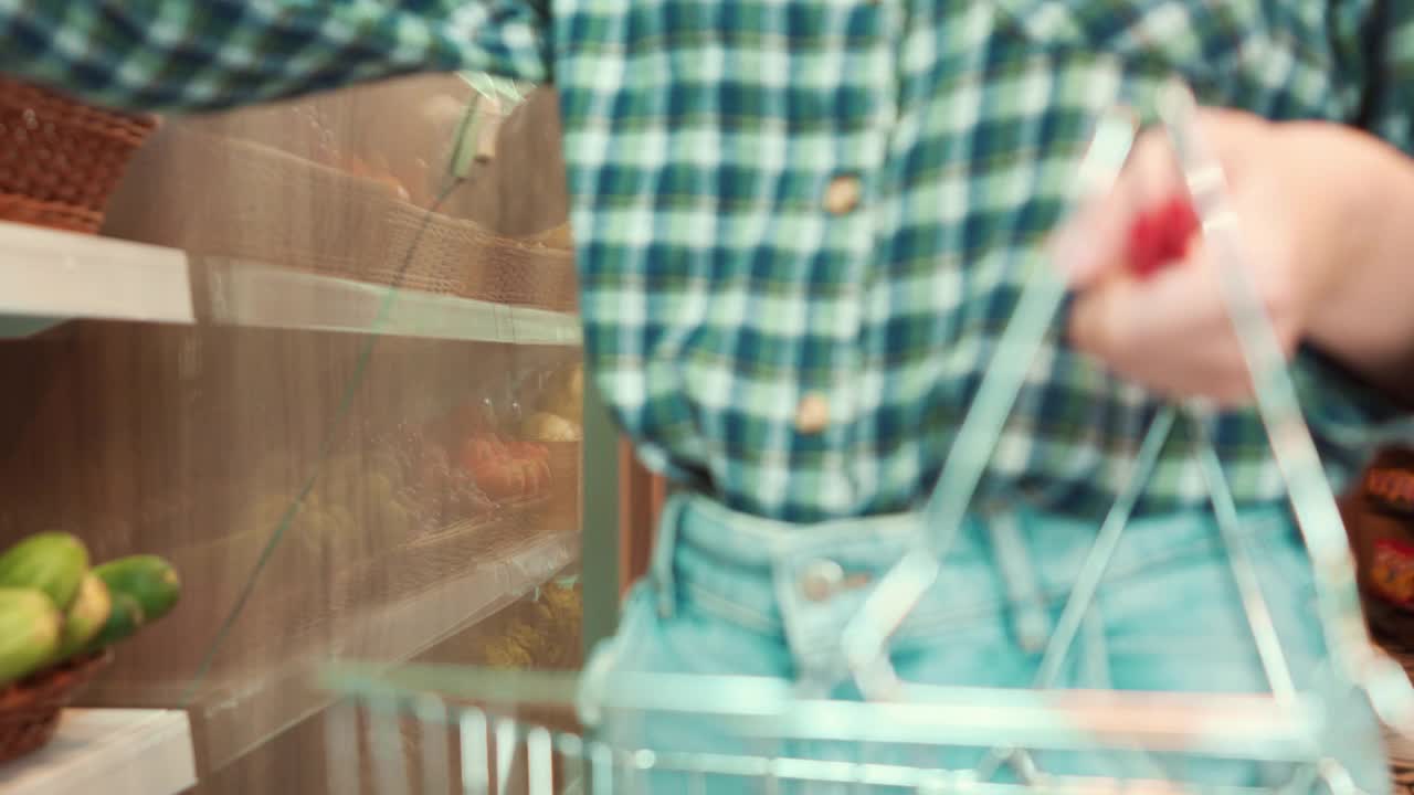 一名年轻的白人妇女正在从货架上拿起橘子和苹果，把它们放在购物篮里准备结账。视频素材